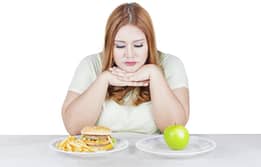 Femme obèse hésitante devant une assiette de gaufres et une pomme.