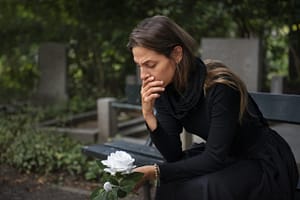 Photo illustrant une femme endeuillée, habillée en noir, devant une tombe.